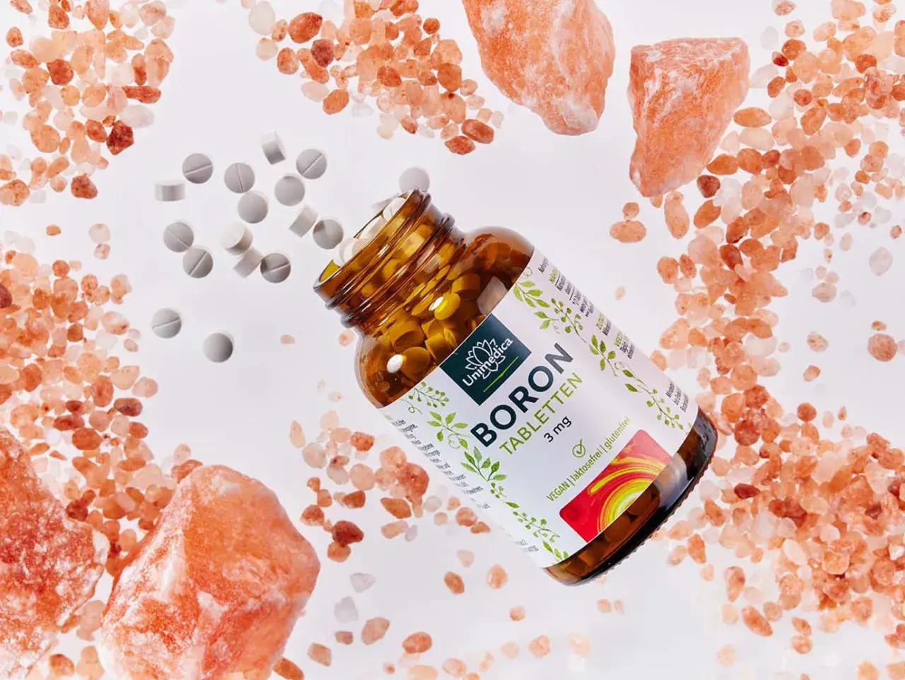 Braune Glasflasche mit BORON Tabletten, umgeben von rosa Salzkristallen und verstreuten Tabletten. Ein natürliches bor vitamin für Ihr Wohlbefinden.