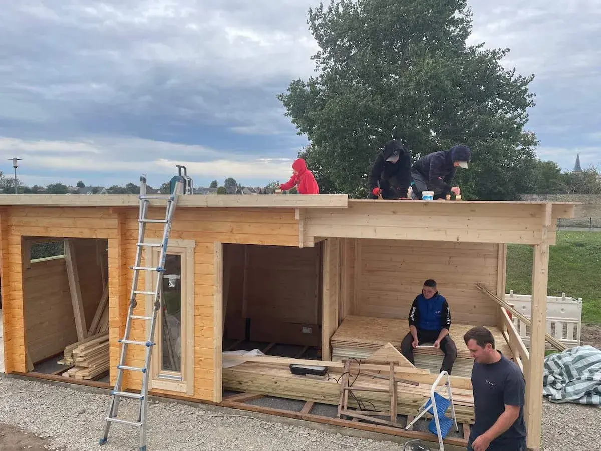 Arbeiter erneuern das **Gartenhaus Dach**. Eine Leiter steht bereit, während mehrere Personen auf dem Dach arbeiten.
