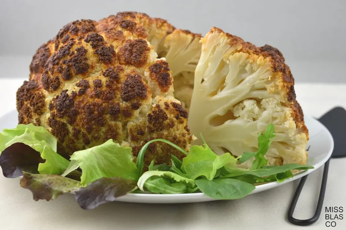 Coliflor al horno, dorada y tierna, servida con una fresca ensalada verde. Un plato saludable y delicioso.