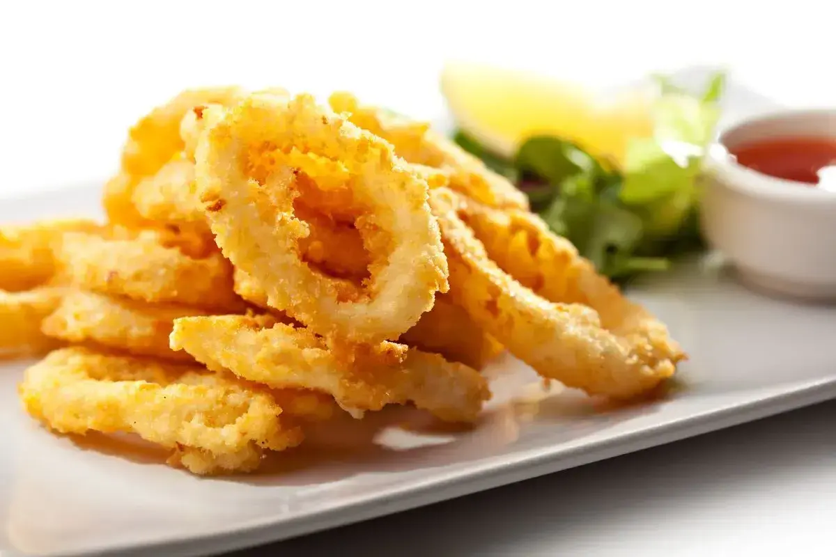 Anelli di totano dorati e croccanti, cotti in friggitrice ad aria, serviti su un piatto bianco con contorno di insalata e salsa.