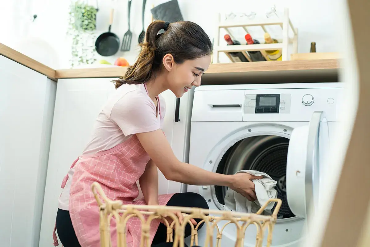 Frau lädt Wäsche in die Waschmaschine. Sie fragt sich, wie oft Jeans waschen, um sie frisch zu halten.