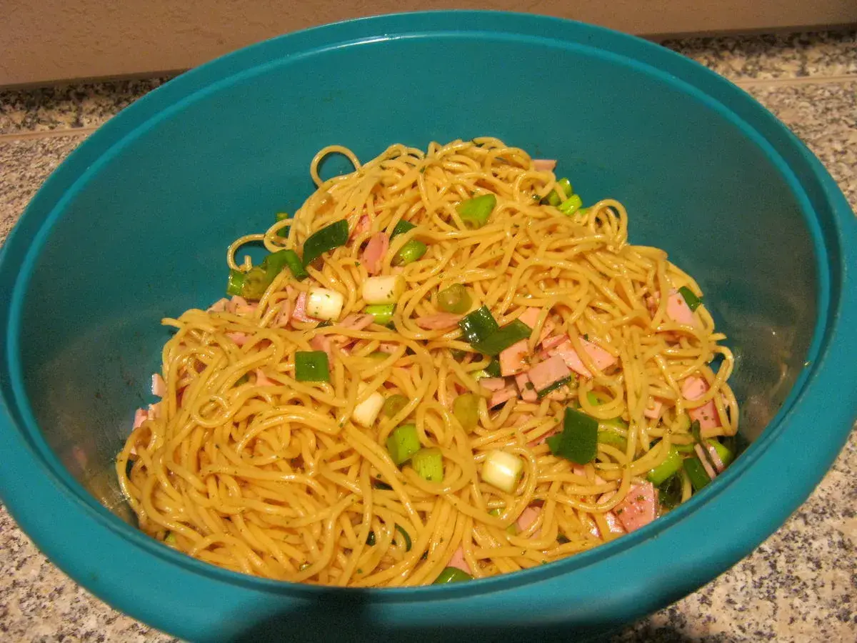 Ein leckerer Maggi Salat mit Spaghetti, Schinkenwürfeln und Frühlingszwiebeln in einer blauen Schüssel.