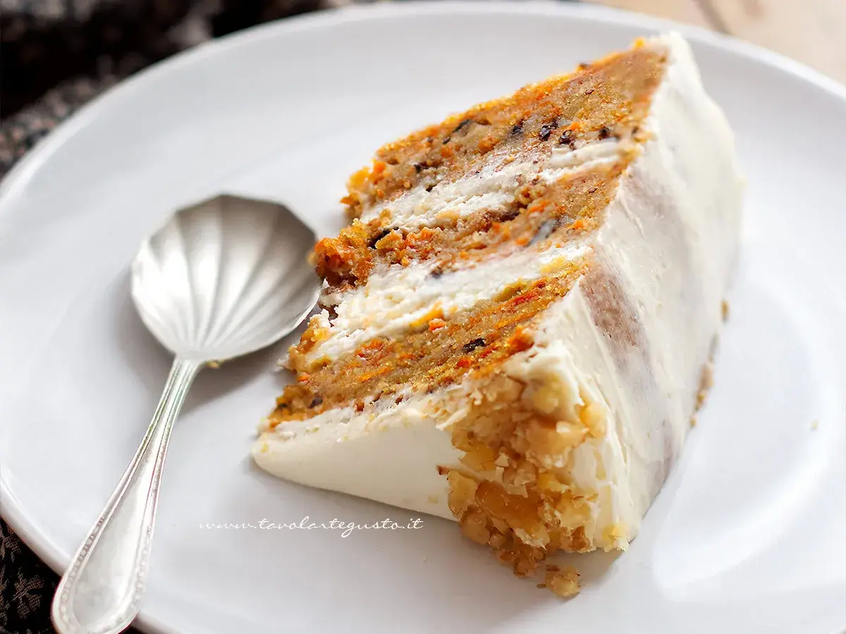 Una fetta di torta di carote, soffice e ricca, con glassa bianca e noci tritate.