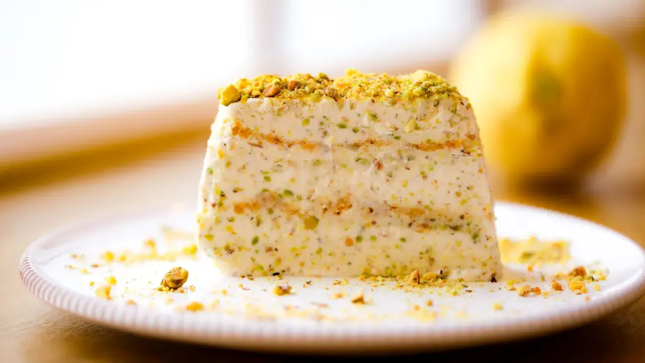 Ein Stück cremiges Semifreddo al Pistacchio, bestreut mit gehackten Pistazien, auf einem Teller.