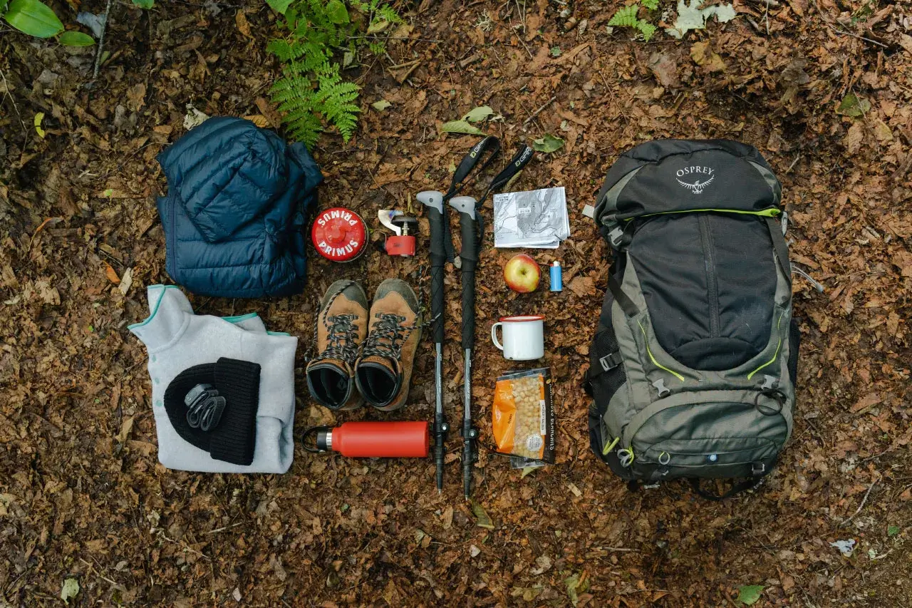 Préparation pour faire son sac de randonnée à la journée : sac à dos Osprey, chaussures, vêtements chauds, bâtons, réchaud, gourde, carte et en-cas.