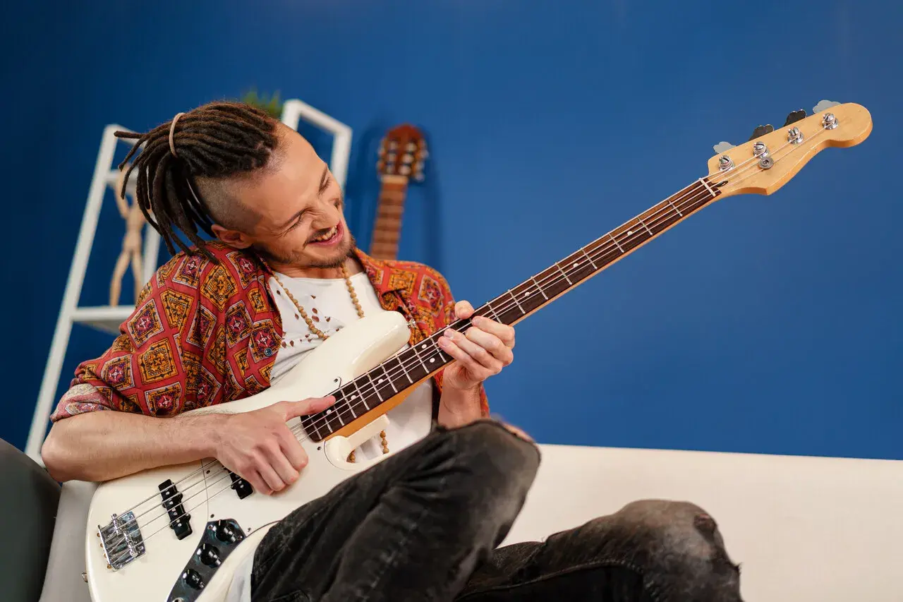 Mężczyzna z dredami gra na białej gitarze basowej. Ile strun ma gitara basowa? Ta ma cztery.