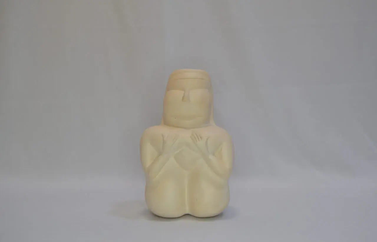 Figurina stilizzata che evoca la dea madre sarda, con mani giunte sul petto e un'espressione serena.