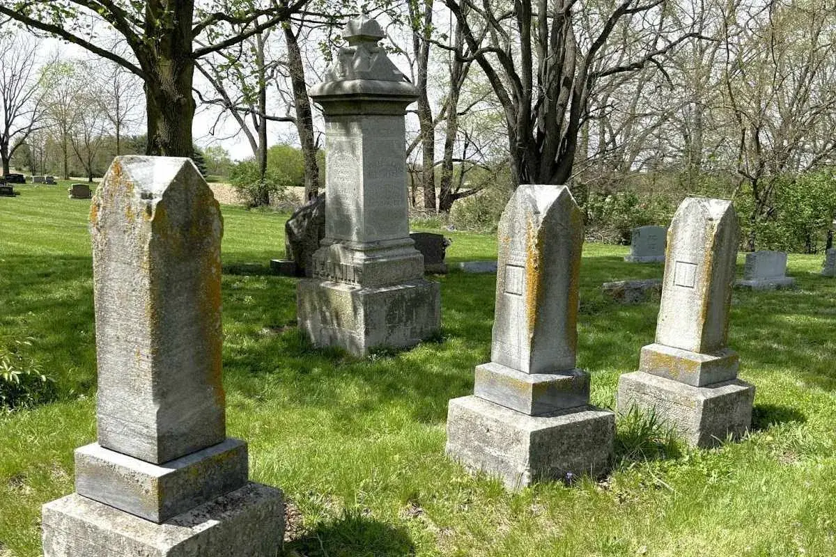 Vieilles pierres tombales dans un cimetière verdoyant, sous des arbres feuillus. Un lieu paisible pour se souvenir.