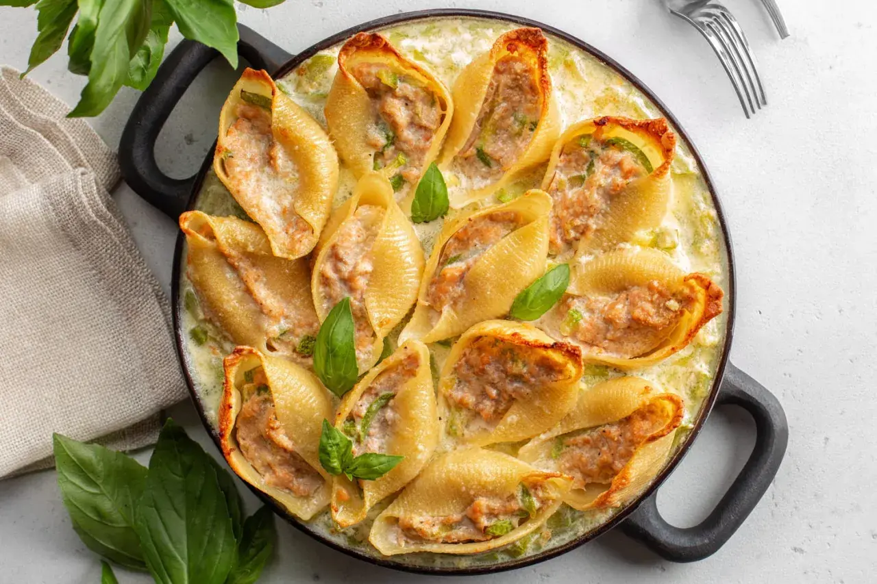 Un plat de conchiglioni farcis, dorés et garnis d'une farce savoureuse, baignant dans une sauce crémeuse et décorés de feuilles de basilic frais.