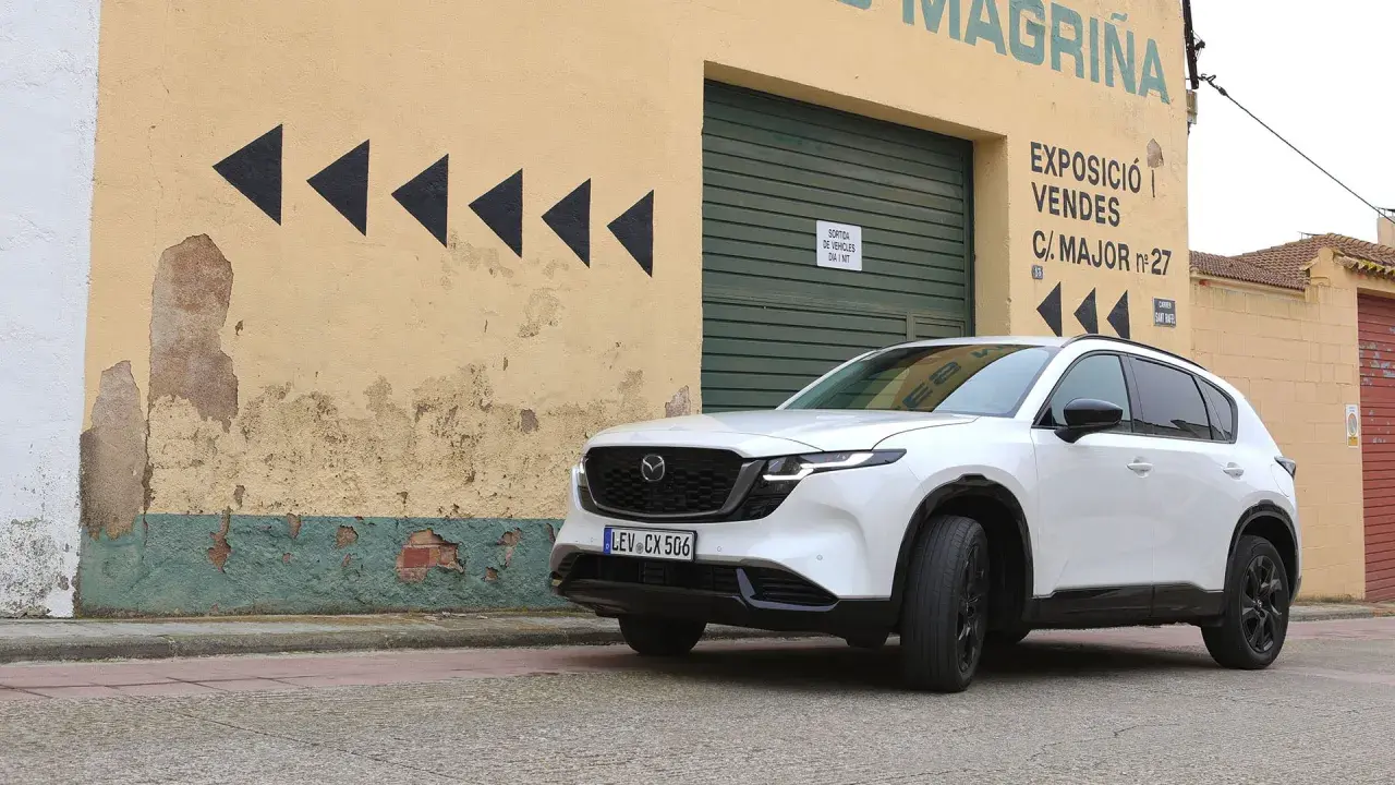 Vit Mazda CX-5 framför en sliten gul byggnad med svarta pilar. Kanske ett Mazda CX-5 problem med att hitta rätt väg?
