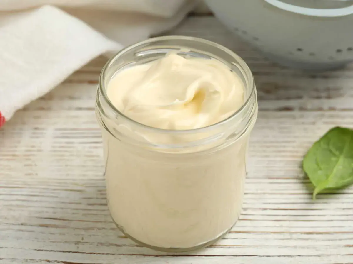 Un pot en verre rempli d'une onctueuse mayonnaise sans huile, sur une table en bois. Une feuille verte à côté.