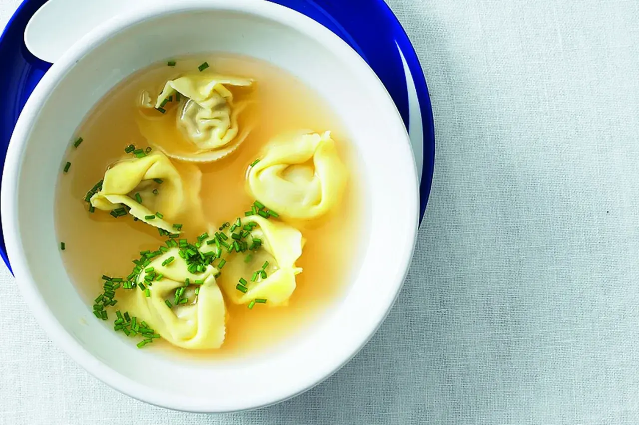 Eine Schüssel mit Tortellini in Brühe, garniert mit Schnittlauch.