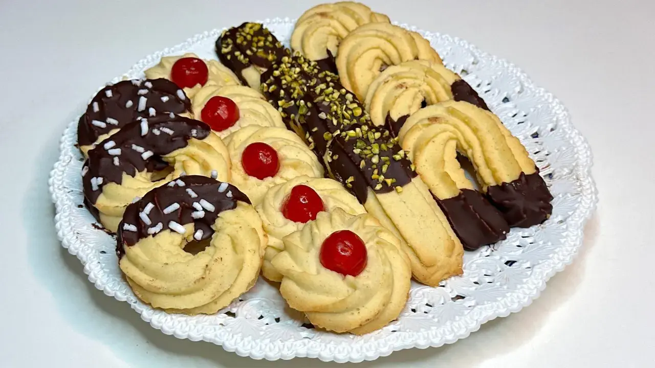 Vassoio di frolla montata: biscotti decorati con cioccolato, granella di pistacchio e ciliegie candite.
