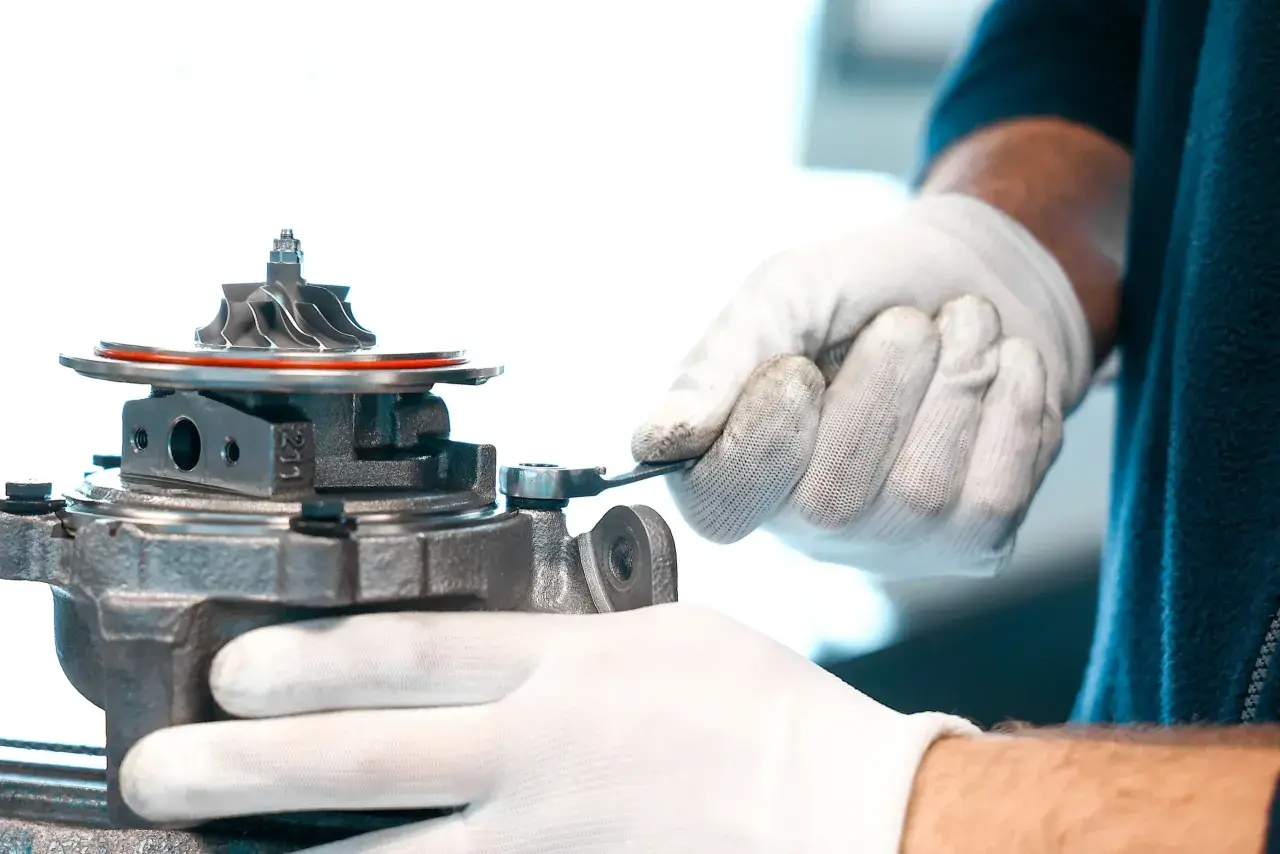 Mechanik w białych rękawiczkach dokręca śrubę przy turbosprężarce, być może regulując zawór N75.