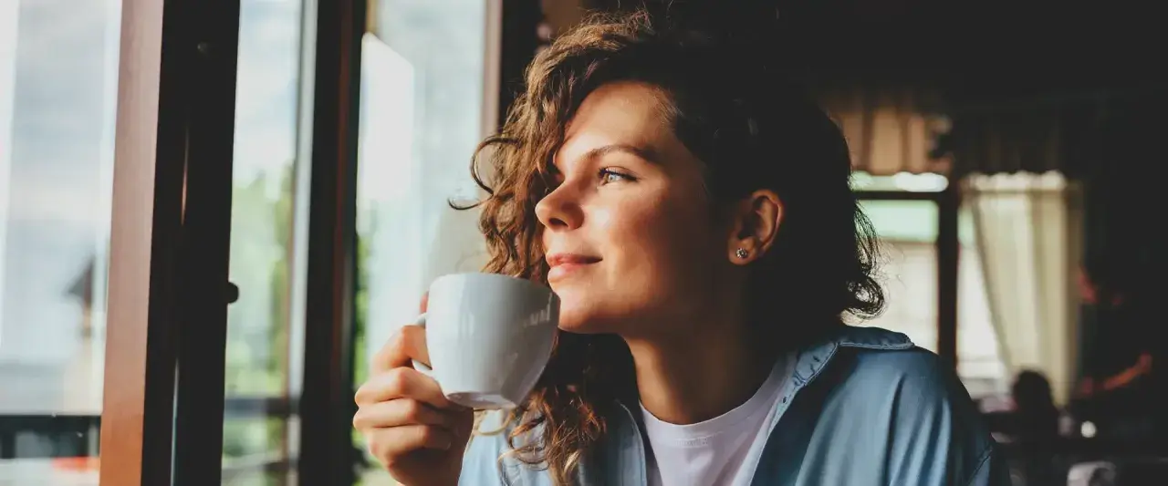 Frau mit lockigen Haaren genießt eine Tasse Chai Latte, ein Moment der Ruhe während der Schwangerschaft.