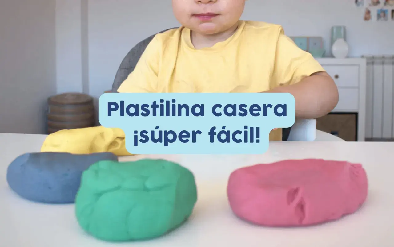 Un niño sonriente listo para jugar con plastilina casera para niños de colores: azul, verde, amarillo y rosa.