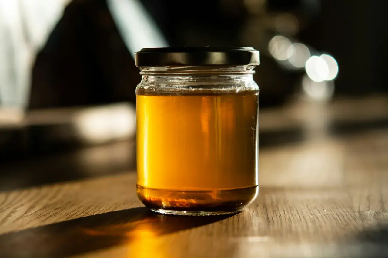 Słoik złocistego miodu na drewnianym stole. Czy miód nawilża gardło? Ten naturalny produkt może przynieść ulgę.