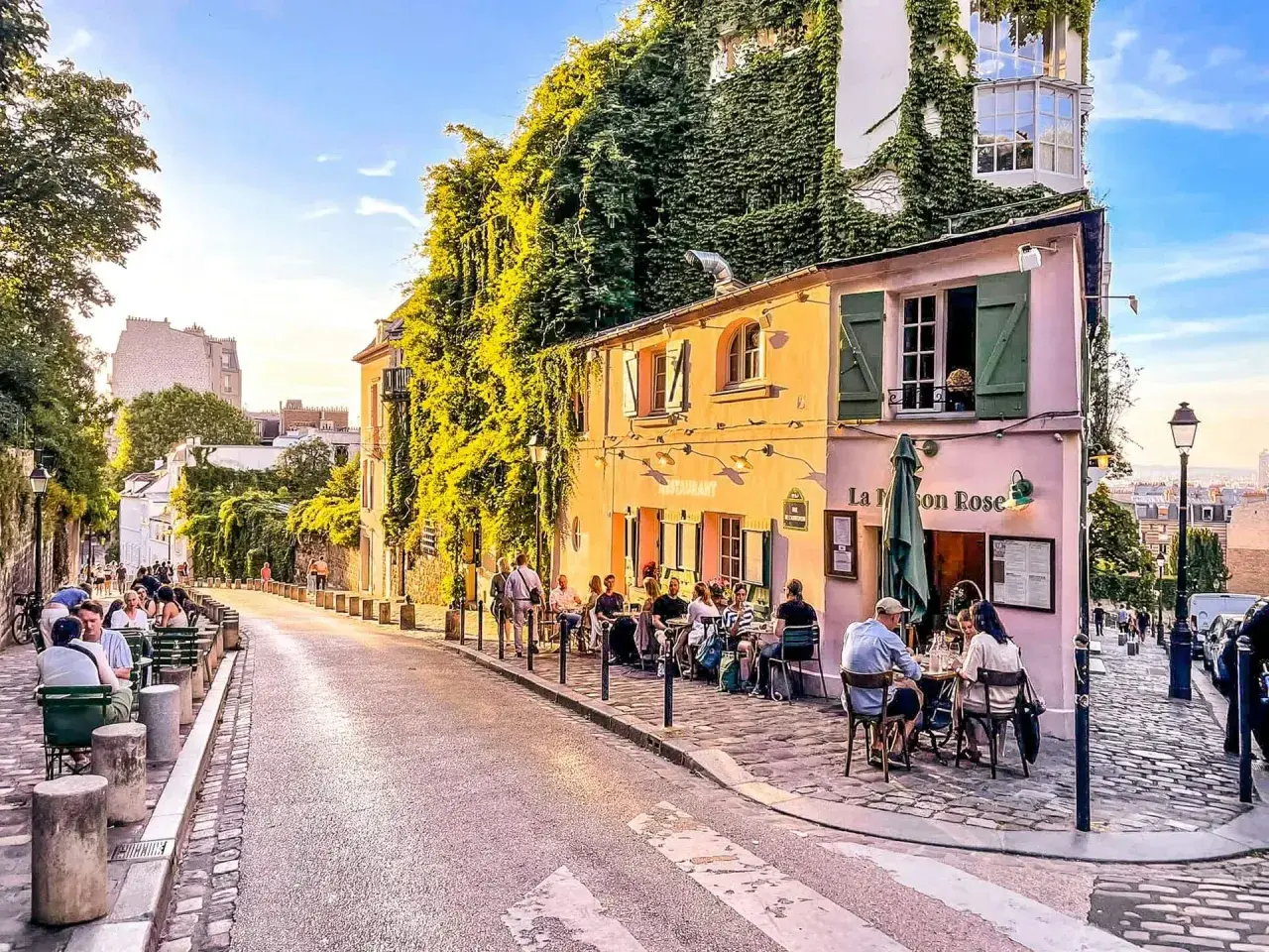 Ulica na Montmartre, z kawiarnią La Maison Rose i ludźmi siedzącymi przy stolikach.