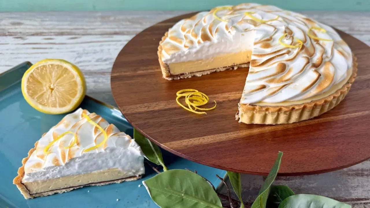 Ein köstliches Zitronentarte Rezept: Ganze Tarte und ein Stück mit Baiserhaube, garniert mit Zitronenzesten.