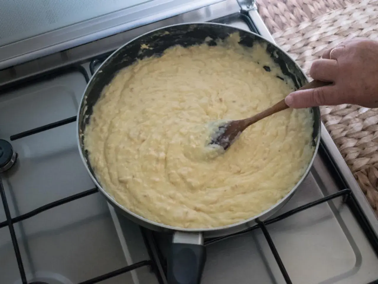 Masa de croquetas cremosa en sartén, removida con cuchara de madera.