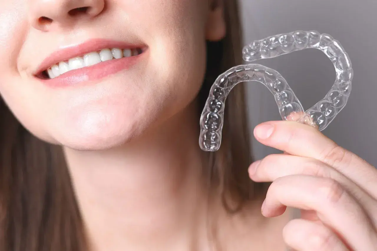 Una persona sonríe mostrando sus dientes y sostiene un alineador transparente. Invisalign para que sirve: para corregir la alineación dental de forma discreta.