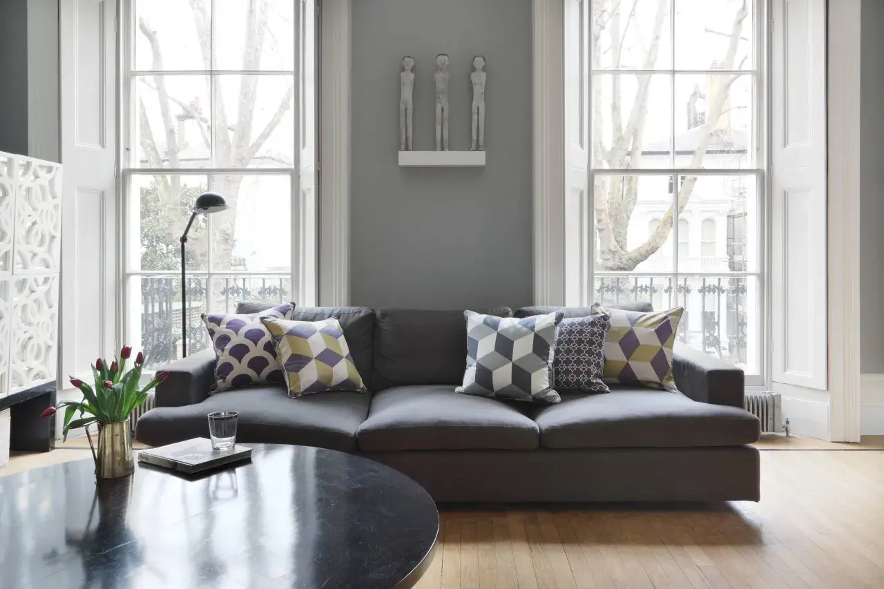 Graues Sofa mit Kissen in Lila, Gelb und Grau. Die Farben passen gut zu Grau und schaffen eine gemütliche Atmosphäre.