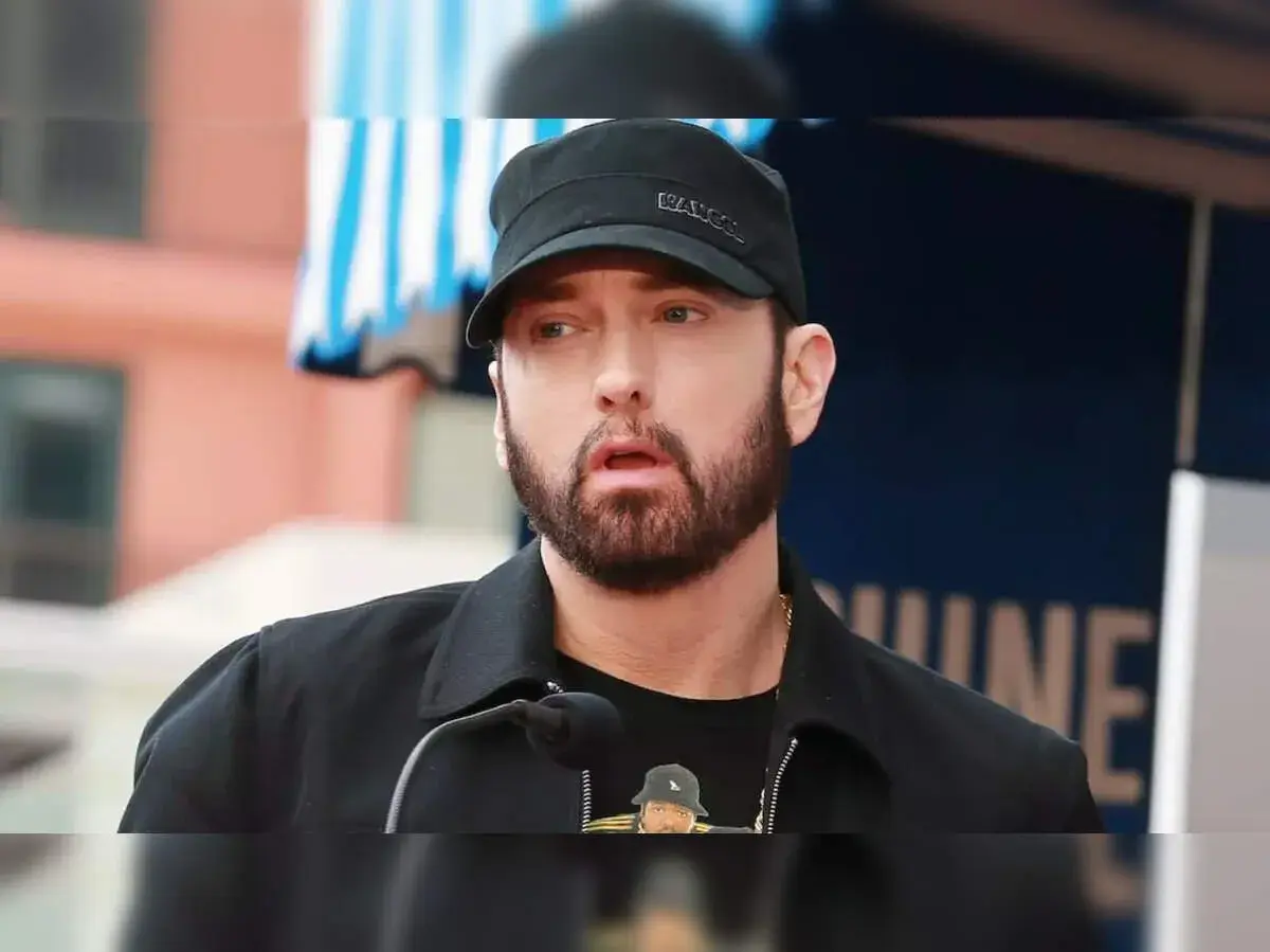 Eminem, znany jako "mockingbird po polsku", w czapce i z brodą, przemawia do mikrofonu.