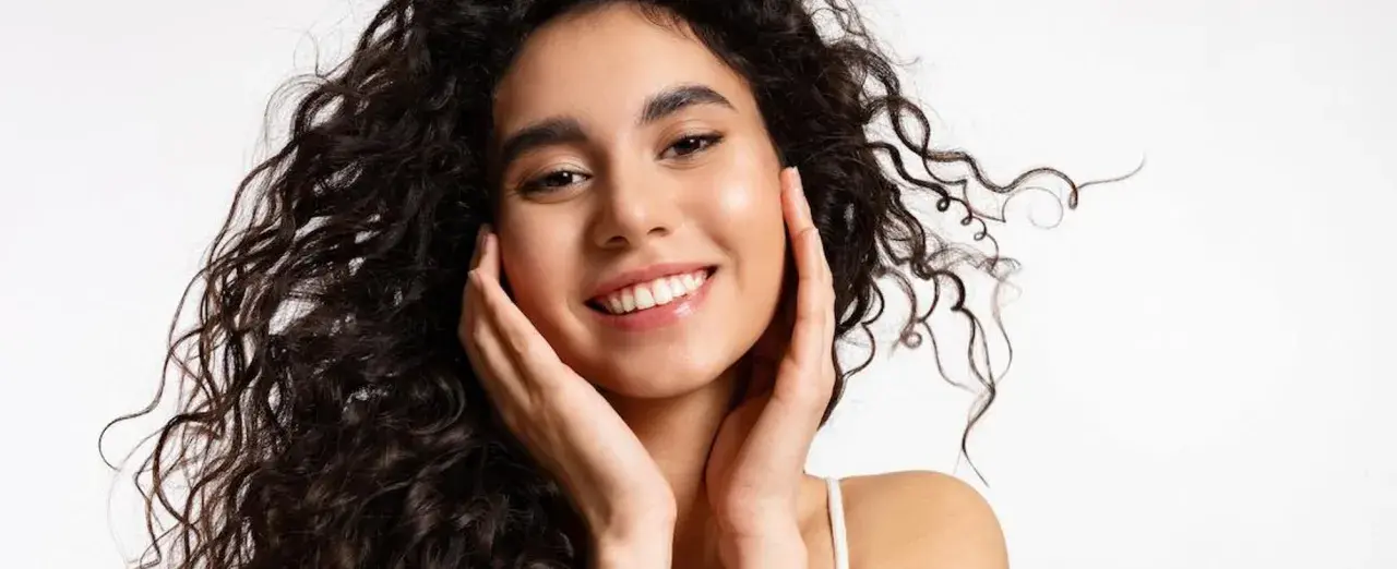 Sonrisa radiante con un toque de strawberry makeup, cabello rizado oscuro y piel luminosa.