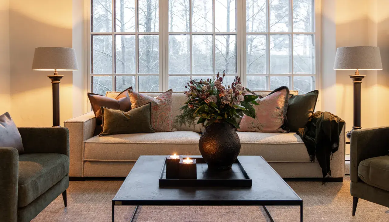 Mysig lounge med soffa och gröna artwood fåtöljer. Blommor, ljus och en filt skapar en varm atmosfär.