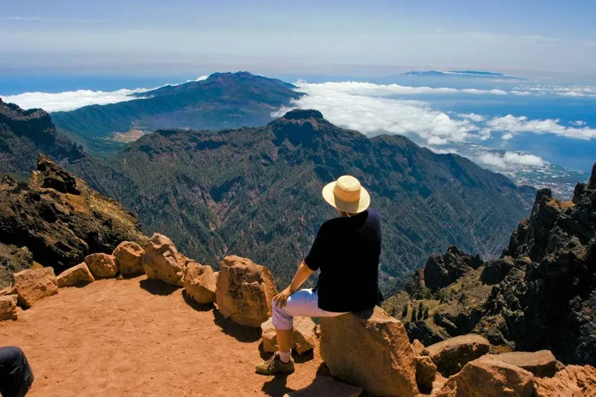 Persona con sombrero admira el paisaje montañoso y el mar, disfrutando de las **rutas La Palma**.