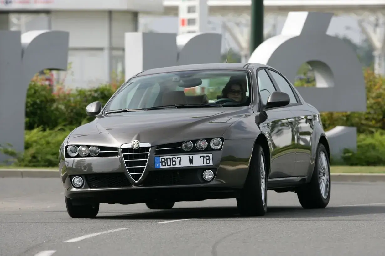 Eleganckie Alfa Romeo 159 2.4 JTDm w kolorze grafitowym, z kobietą za kierownicą, jedzie po drodze.