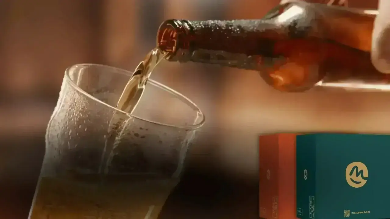 Versando una hefe birra dorata in un bicchiere bagnato. Sullo sfondo, due scatole colorate con il logo "m".