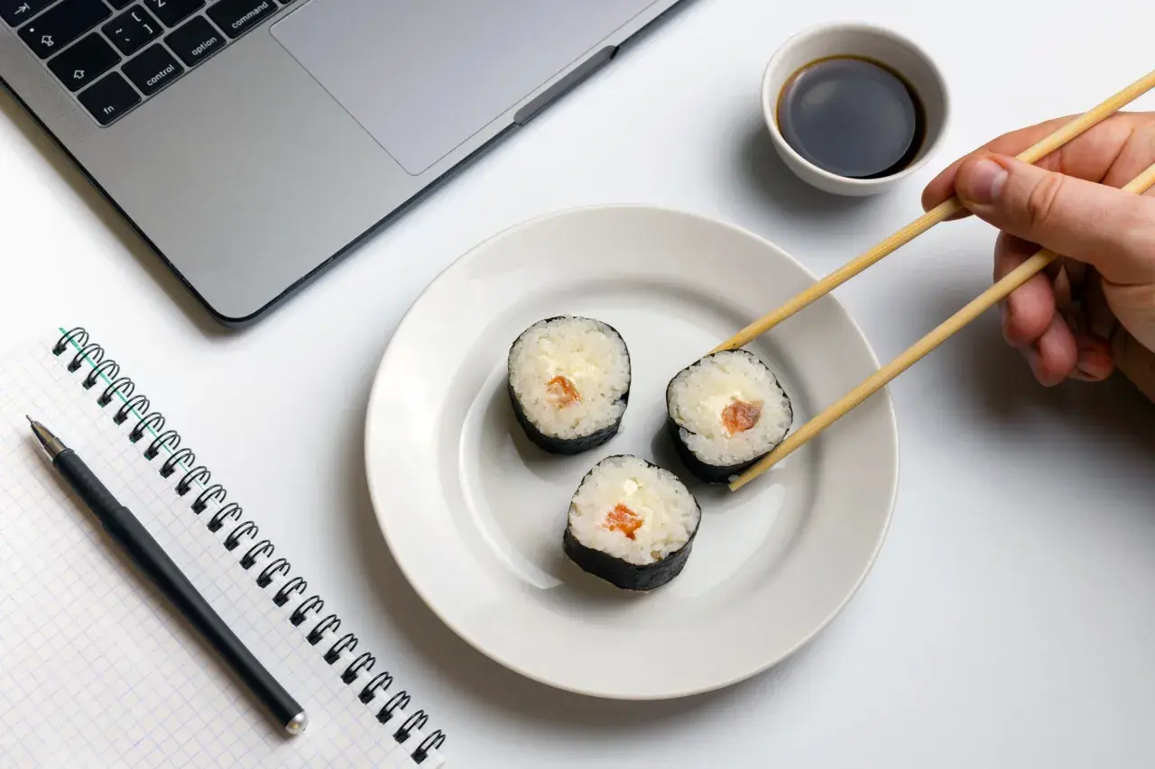 Praca i zdrowie idą w parze. Na biurku laptop, notatnik i pałeczki do sushi, idealne dla zwolenników peskatarianizmu.
