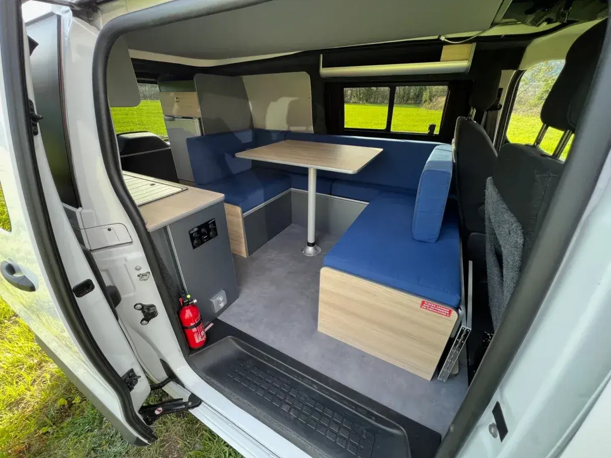 Aménagement intérieur d'un camping-car : banquettes bleues, table, coin cuisine. Idéal pour construire son camping car.