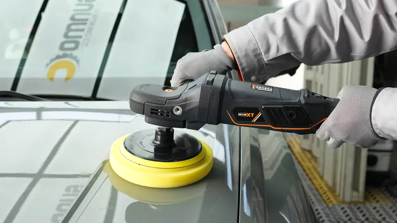 Persona con guantes usa una pulidora para detallar el capó de un coche gris.