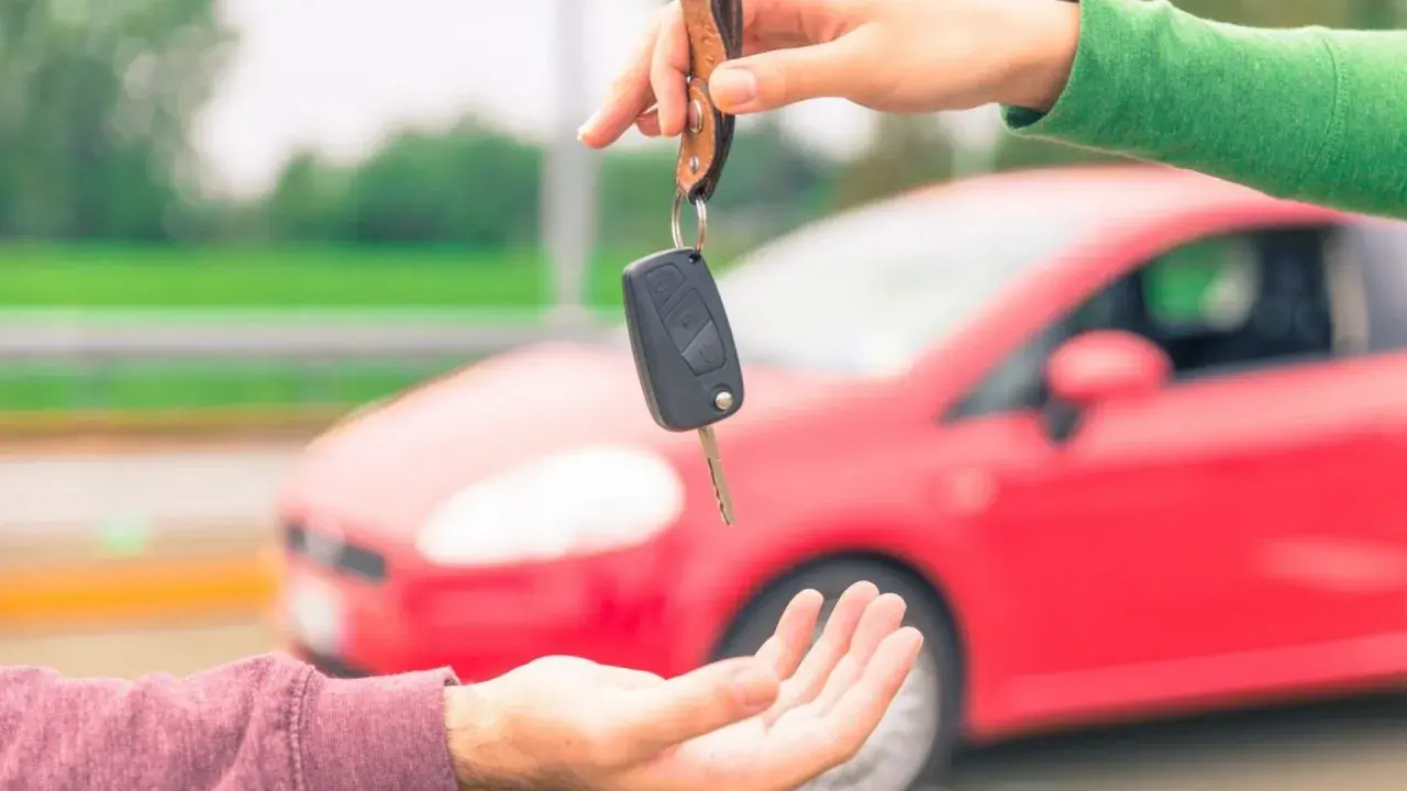 Passaggio di chiavi per vendere l'auto velocemente. Una mano porge le chiavi di un'auto rossa a un'altra mano.