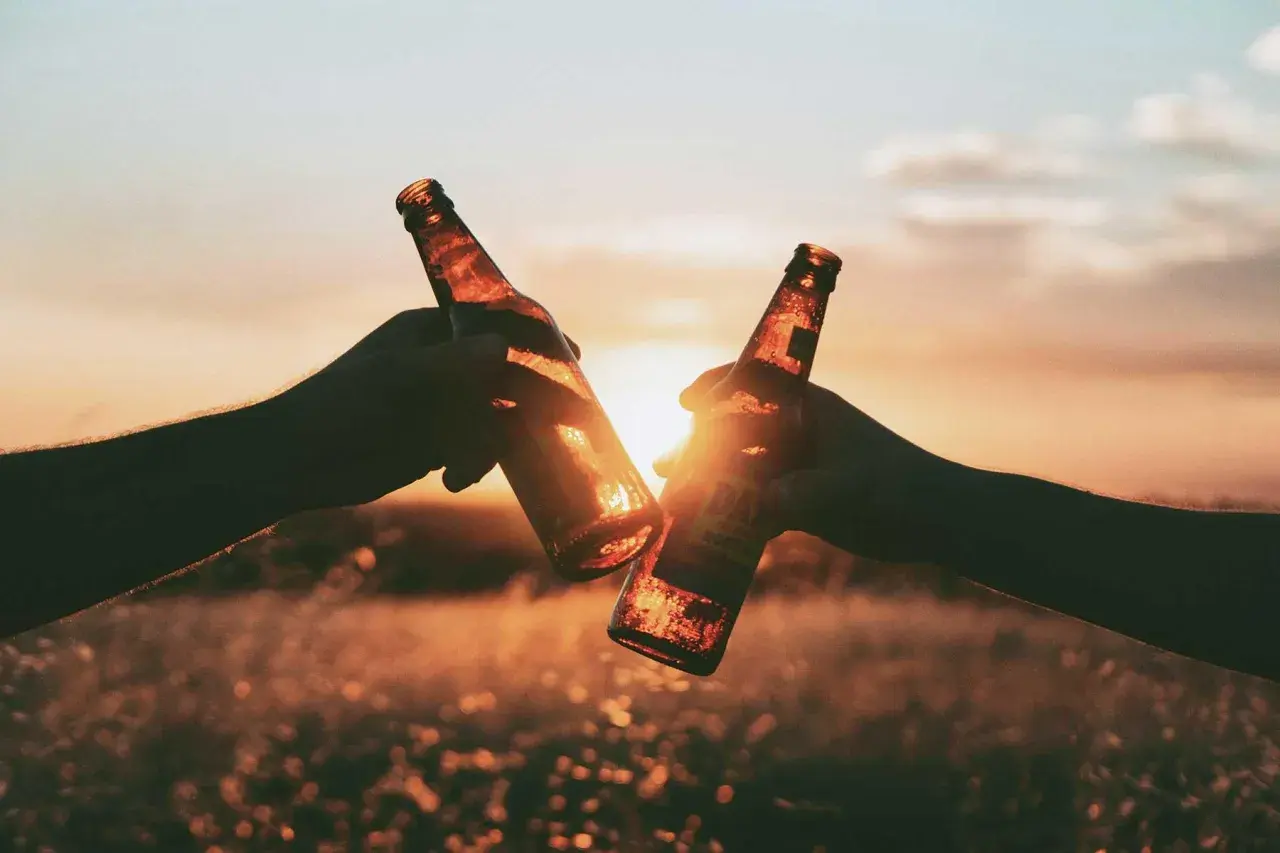 Due mani brindano con due bottiglie di birra al tramonto, un meritato momento di relax dopo un allenamento.