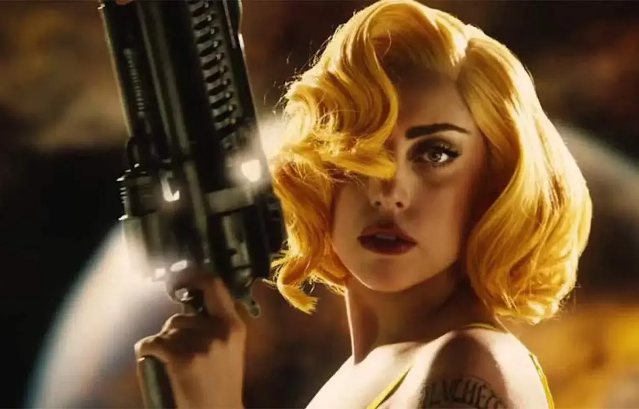 Lady Gaga med blont hår och en futuristisk pistol i en scen från en av hennes filmer.