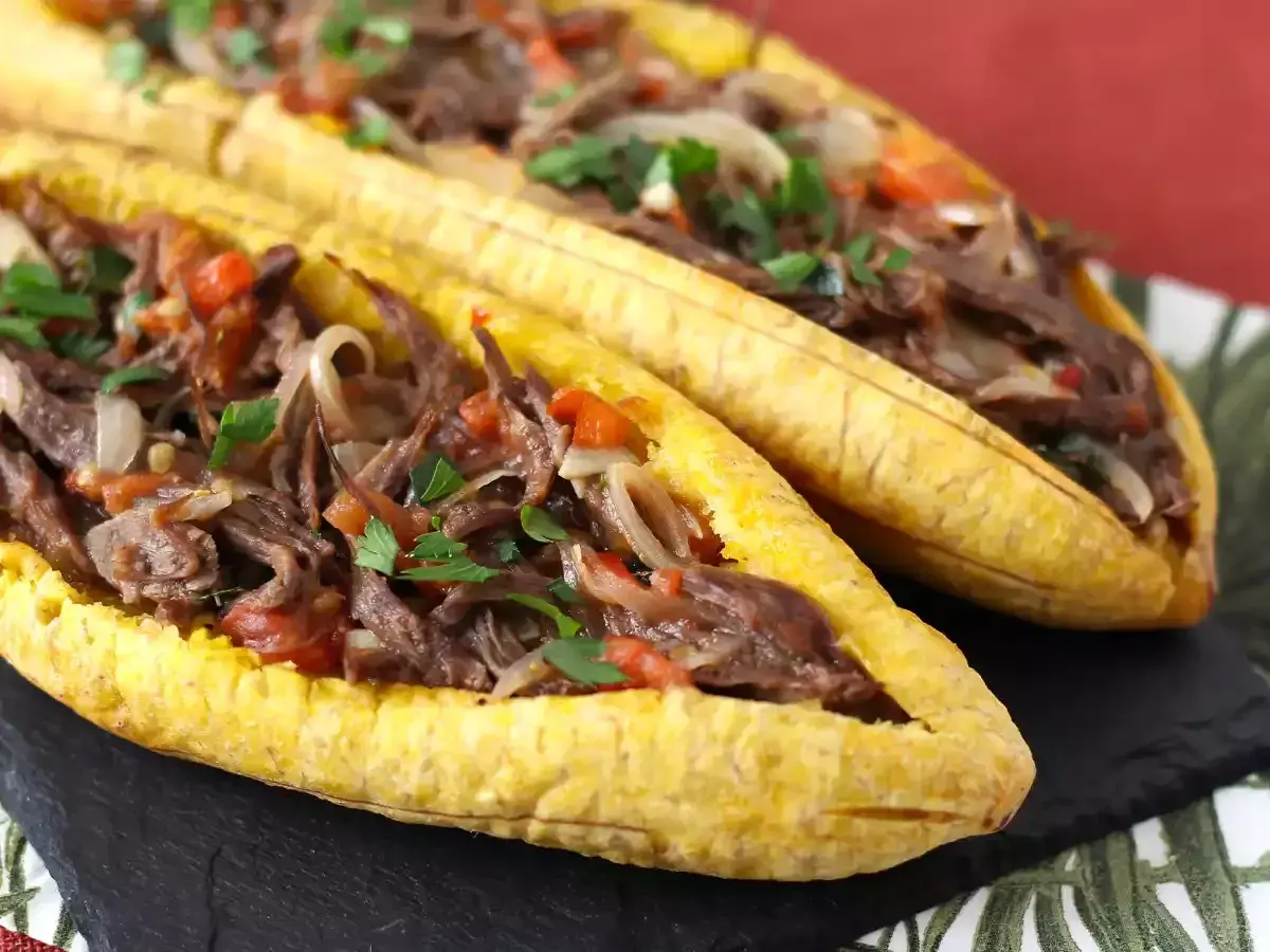 Deux bananes plantain farcies d'un ragoût de bœuf effiloché, d'oignons et de tomates, garnies de persil frais.