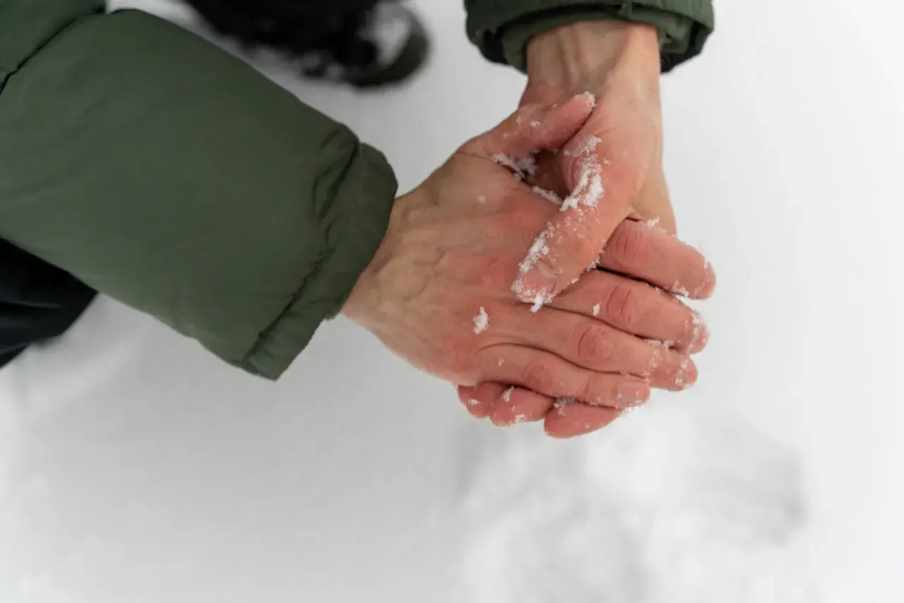 Händer med snö på, som gnuggas mot varandra för att värma upp torra handflator.