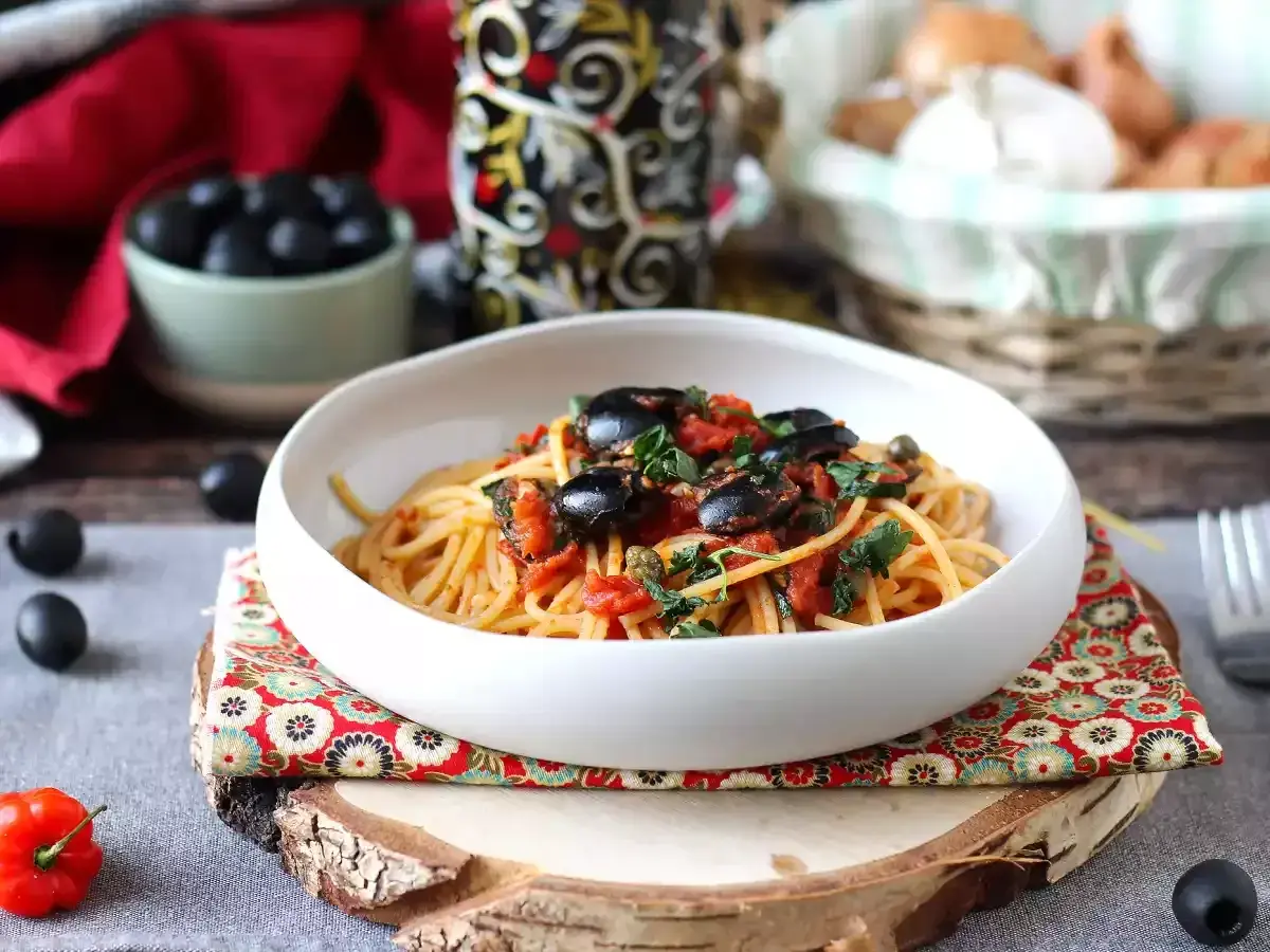 En skål med spaghetti puttanesca, toppad med svarta oliver och persilja. Ett härligt recept för en smakrik middag.