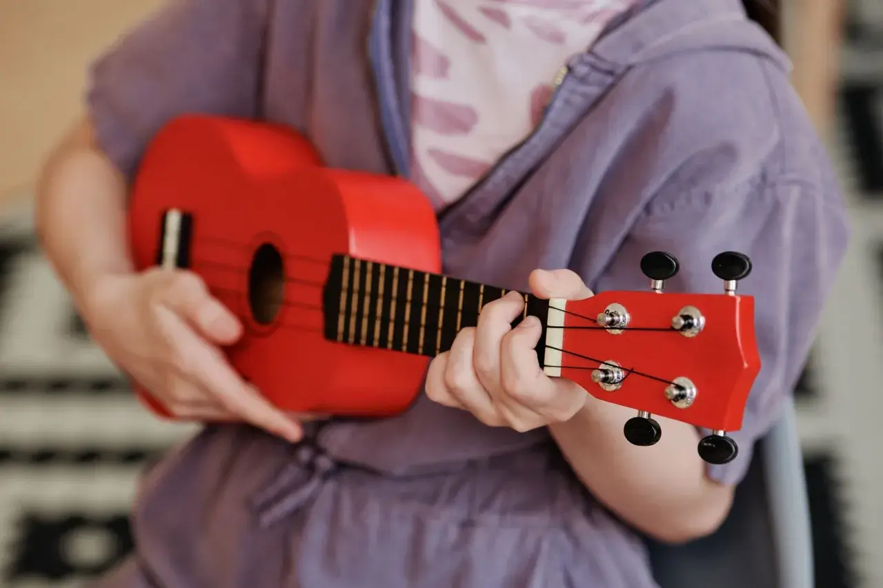Enfant jouant d'un petit instrument de musique rouge vif, un ukulélé, avec concentration.