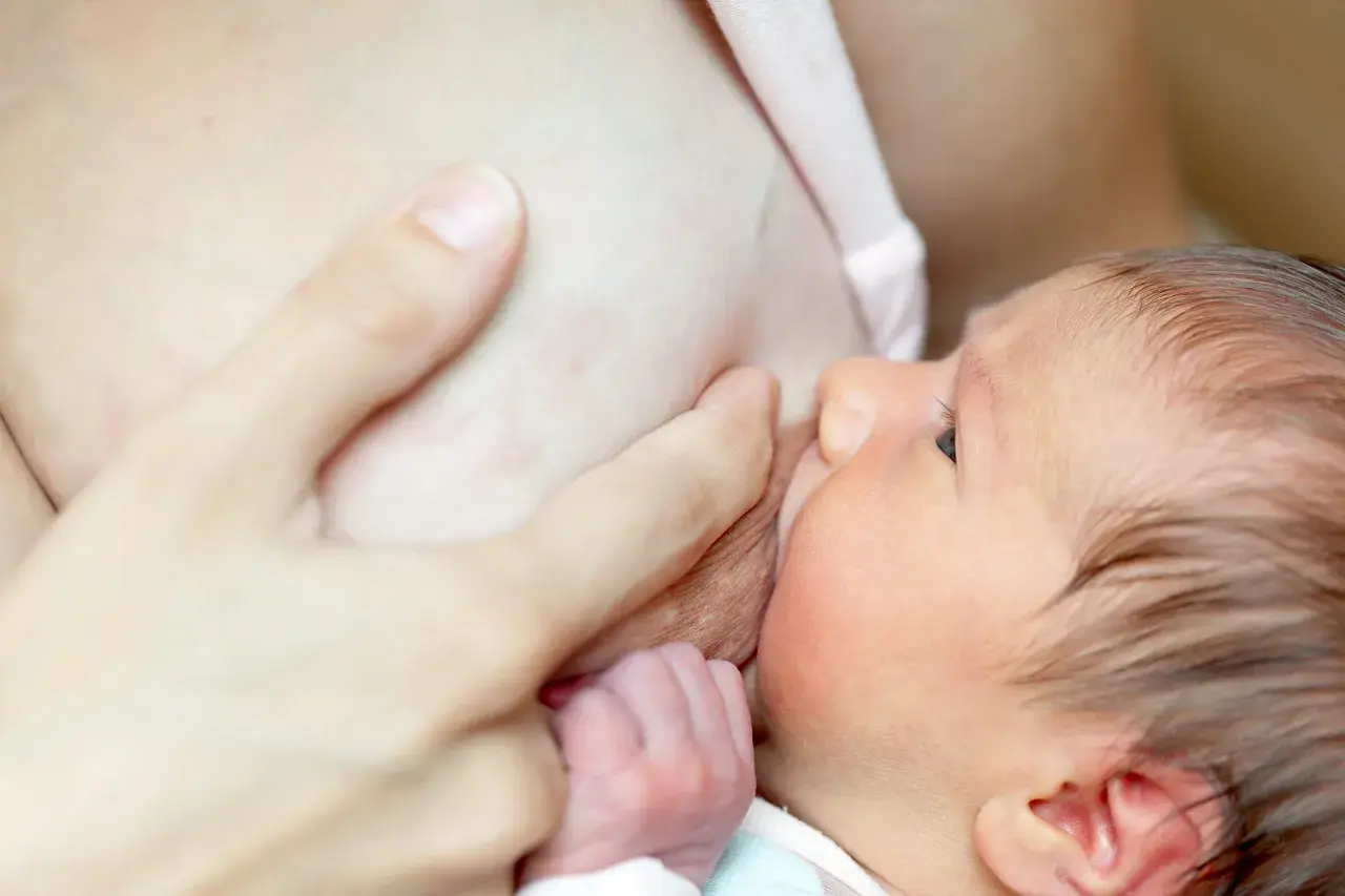 Un bébé tète le sein de sa mère. Une main soutient le sein, peut-être pour soulager les symptômes de mastite.