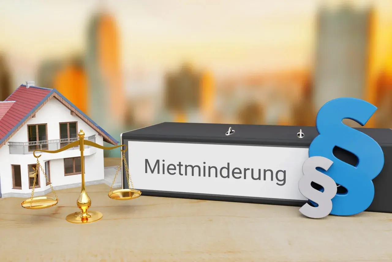 Hausmodell, Waage und Aktenordner mit "Mietminderung" beschriftet. Ein Paragraphenzeichen symbolisiert das Recht bei Mietminderung von Kalt- oder Warmmiete.