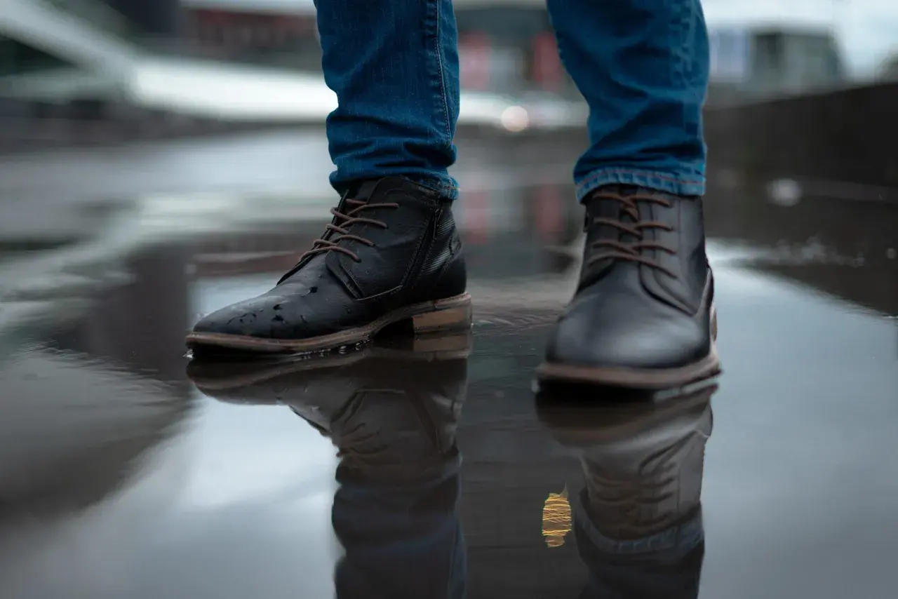 Man in jeans and black boots standing in a puddle. Learn how to rough up the bottom of slippery shoes for better grip.