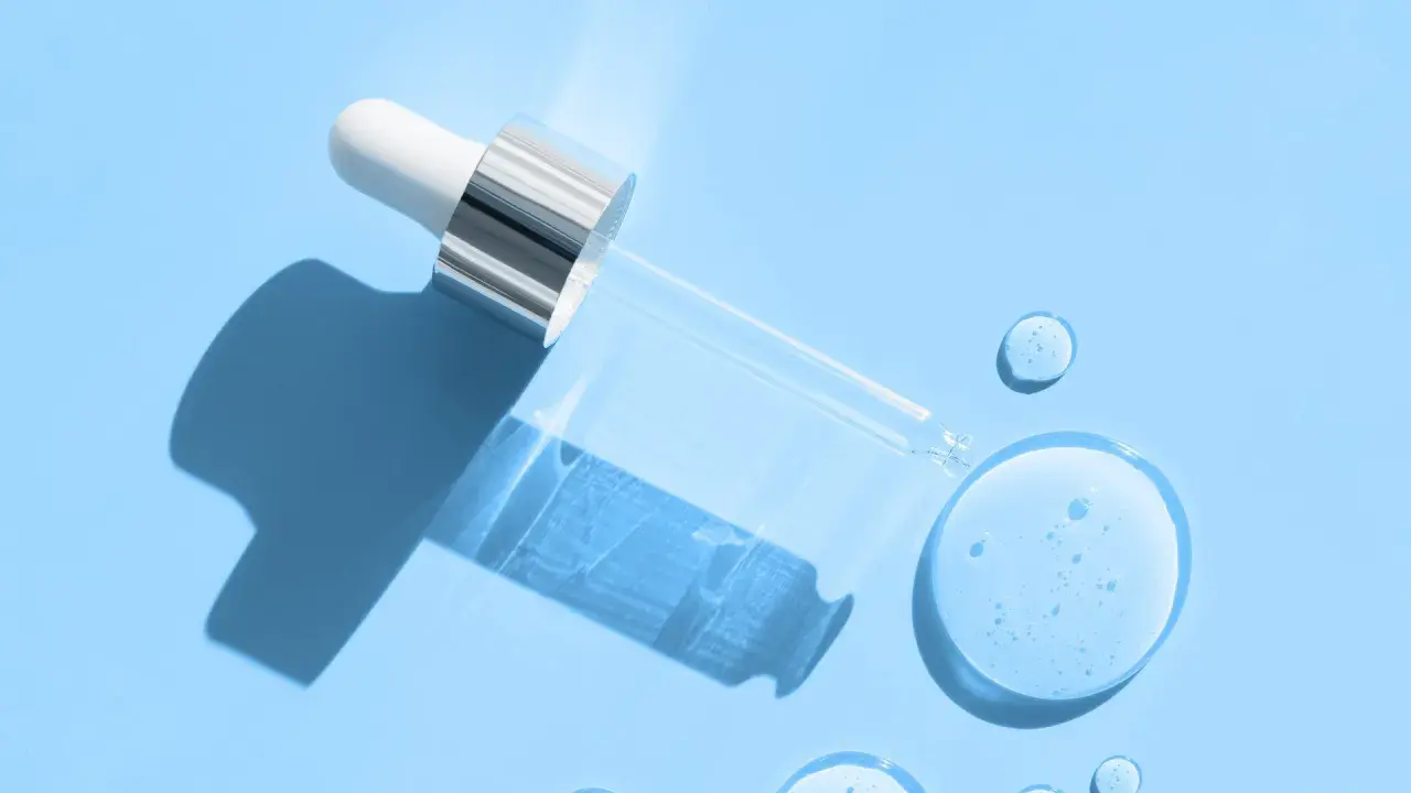 Droppe av serum med hyaluronsyra och retinol på blå bakgrund.