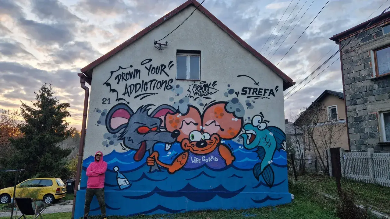 Kolorowy mural na domu jednorodzinnym przedstawia kreskówkowe zwierzęta w wodzie. Widać mysz, małpkę z napisem "LIFE GUARD" i rybę.