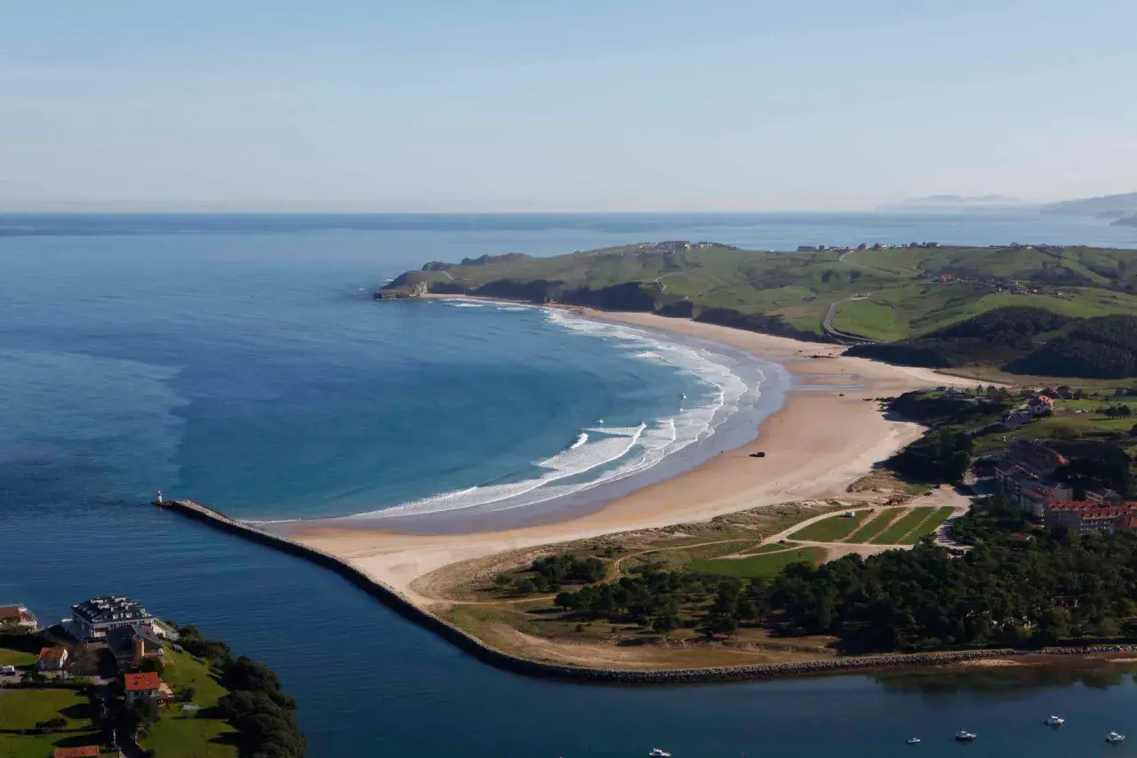 Impresionantes playas cerca de San Vicente de la Barquera, con olas rompiendo en la arena dorada y verdes colinas al fondo.