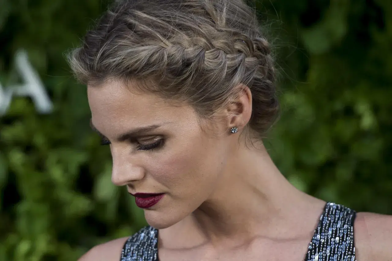 Mujer con elegante peinado con trenzas, maquillaje dramático y vestido brillante.