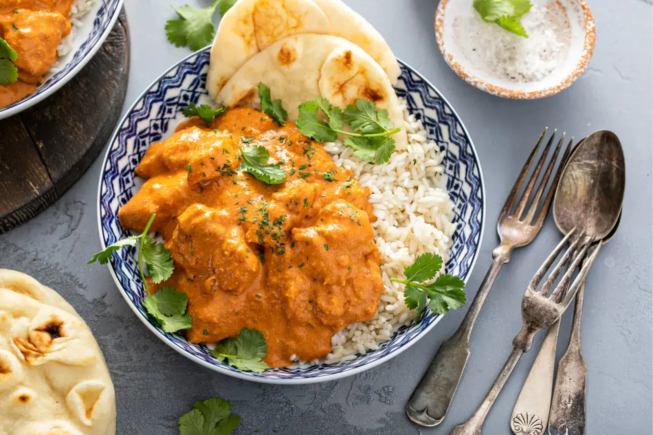 Aksamitny kurczak po indyjsku w pomarańczowym sosie, podany z ryżem basmati i chlebkiem naan. Udekorowany świeżą kolendrą.